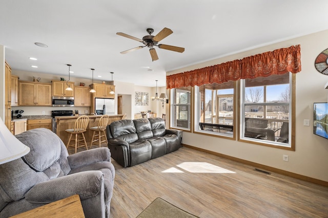 living room featuring visible vents, light wood-style flooring, a ceiling fan, and baseboards