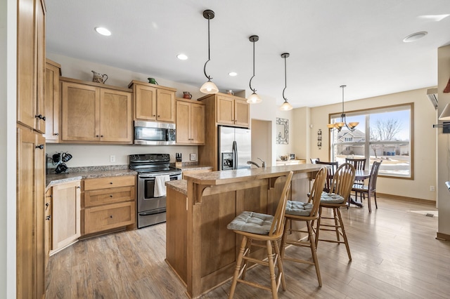 kitchen with stainless steel appliances, a kitchen bar, an island with sink, and light wood-style flooring