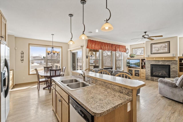 kitchen with a sink, a tiled fireplace, light wood-type flooring, and stainless steel appliances