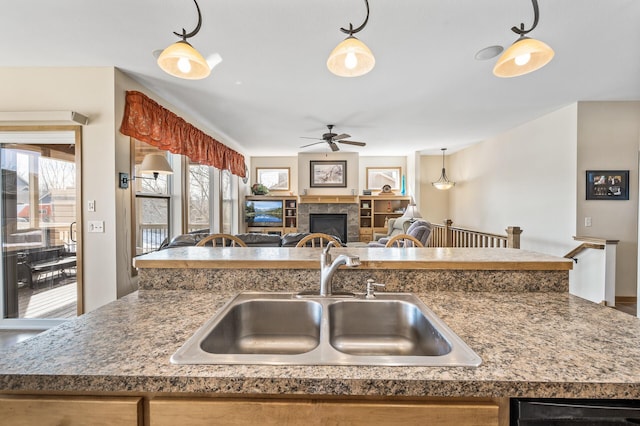 kitchen featuring ceiling fan, decorative light fixtures, open floor plan, a tile fireplace, and a sink