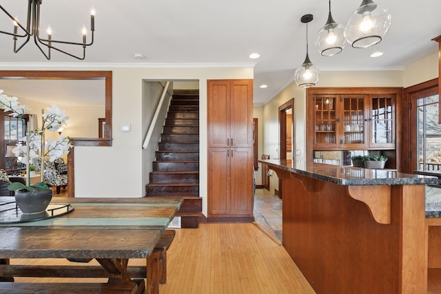 kitchen with brown cabinetry, light wood finished floors, dark stone counters, glass insert cabinets, and a kitchen bar