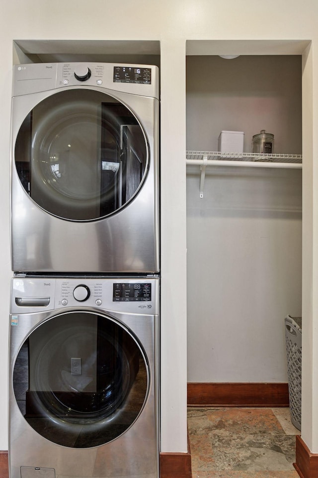 washroom featuring baseboards, stone finish floor, laundry area, and stacked washing maching and dryer