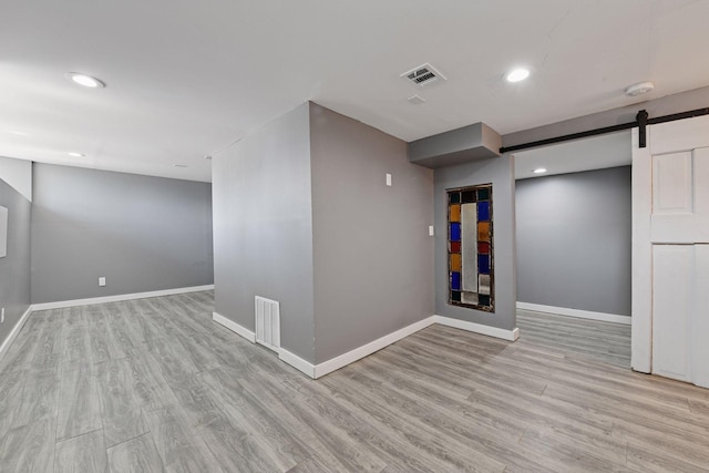 interior space with a barn door, baseboards, visible vents, and wood finished floors