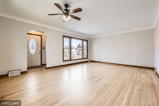 unfurnished living room with visible vents, baseboards, light wood-type flooring, arched walkways, and a ceiling fan