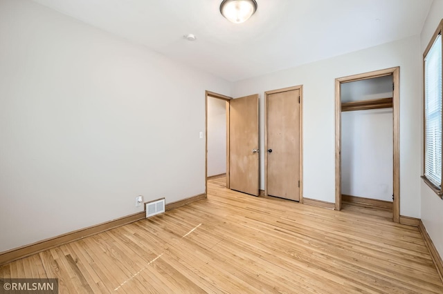 unfurnished bedroom with visible vents, multiple closets, baseboards, and light wood finished floors