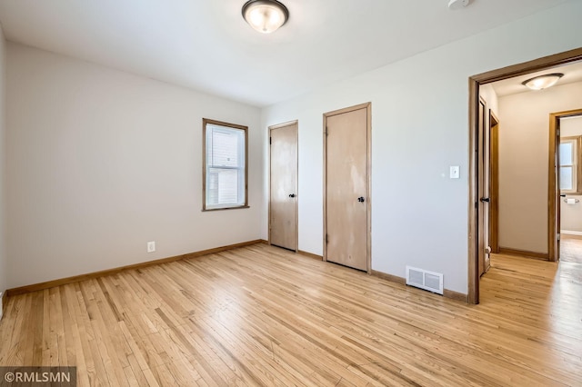 unfurnished bedroom featuring light wood-type flooring, visible vents, multiple closets, and baseboards