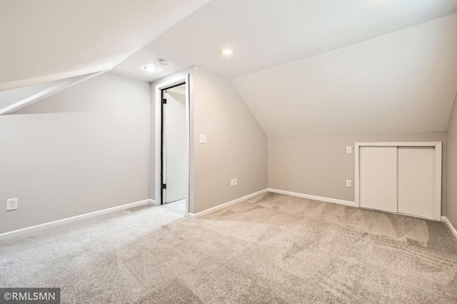 additional living space featuring baseboards, light carpet, and vaulted ceiling