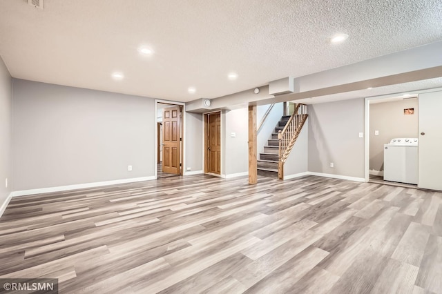 finished basement with light wood-style flooring, a textured ceiling, baseboards, washer / dryer, and stairs