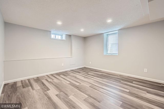 basement featuring a textured ceiling, baseboards, and wood finished floors