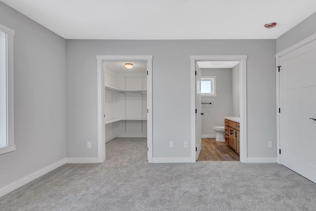 unfurnished bedroom with a walk in closet, carpet flooring, and baseboards