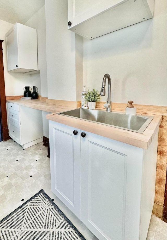 kitchen featuring light floors, white cabinetry, light countertops, and a sink