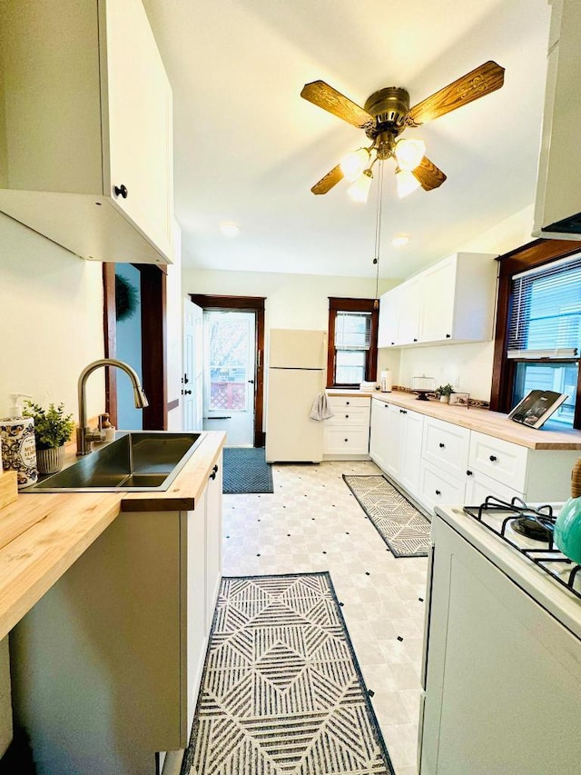 kitchen with butcher block countertops, light floors, white appliances, white cabinetry, and a sink