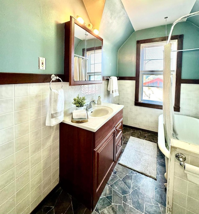 full bath featuring a wainscoted wall, a shower with curtain, tile walls, lofted ceiling, and vanity