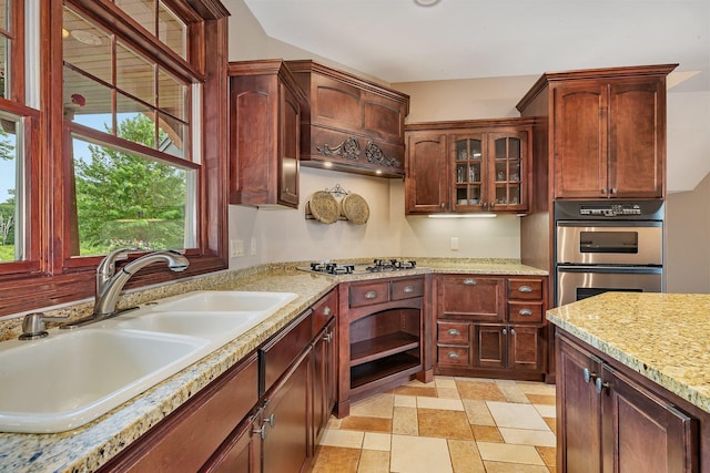 kitchen featuring glass insert cabinets, stainless steel appliances, light stone countertops, and a sink