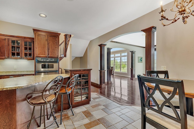 kitchen with arched walkways, glass insert cabinets, ornate columns, and stainless steel oven