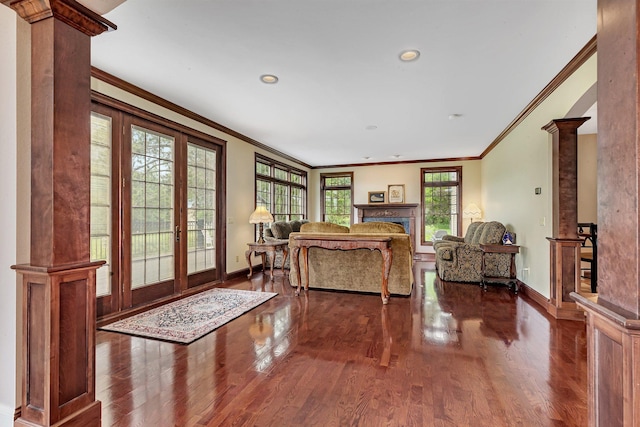 living area with decorative columns, wood finished floors, baseboards, and ornamental molding