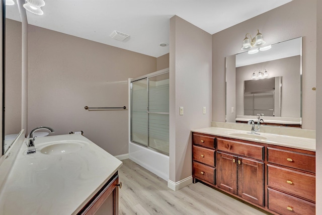 full bathroom with visible vents, wood finished floors, shower / bath combination with glass door, baseboards, and vanity