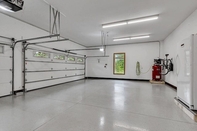 garage with a garage door opener, baseboards, and freestanding refrigerator