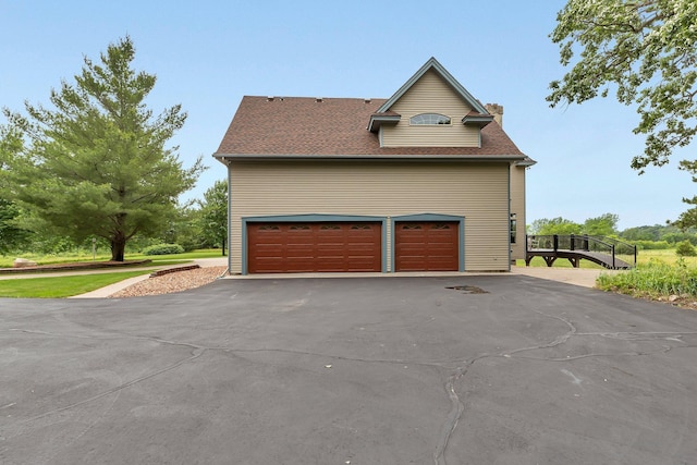 view of side of property featuring a chimney, driveway, and a shingled roof