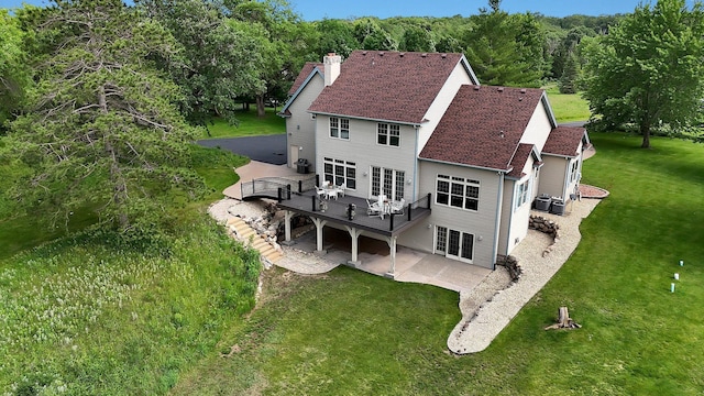 rear view of house with roof with shingles, a lawn, a chimney, a deck, and a patio area