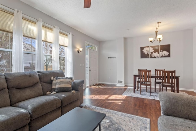 living room with visible vents, ceiling fan with notable chandelier, a textured ceiling, wood finished floors, and baseboards