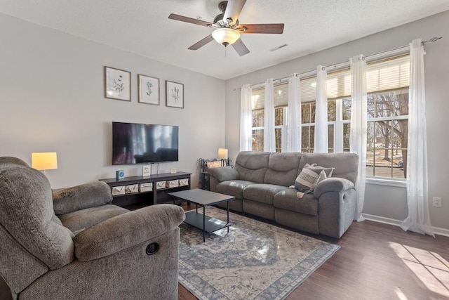 living room featuring baseboards, dark wood-type flooring, a healthy amount of sunlight, and a ceiling fan