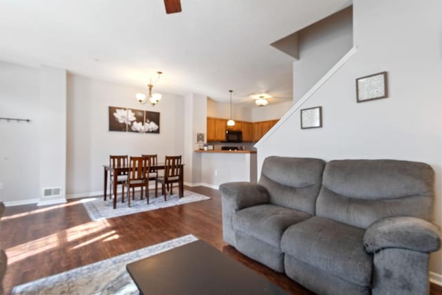 living area featuring dark wood-type flooring, ceiling fan with notable chandelier, visible vents, and baseboards