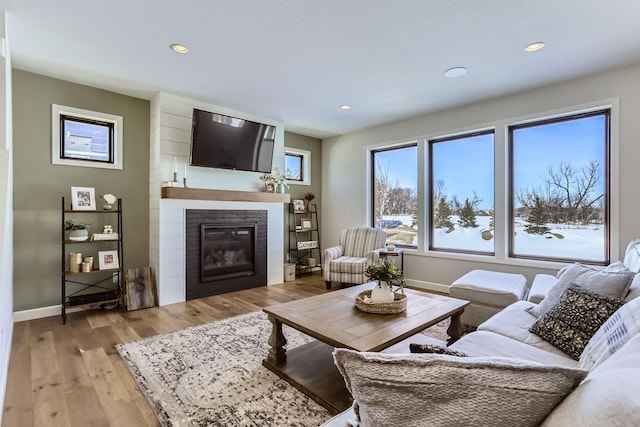 living area with a glass covered fireplace, recessed lighting, baseboards, and light wood-type flooring