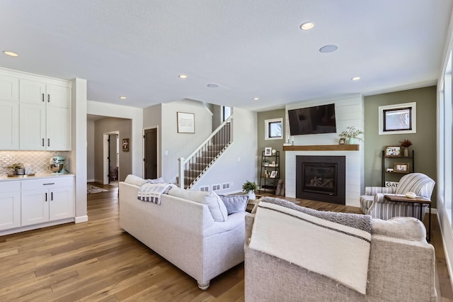 living room with light wood-type flooring, recessed lighting, stairway, a large fireplace, and baseboards