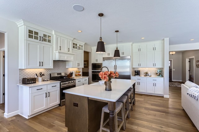 kitchen with under cabinet range hood, built in appliances, wood finished floors, and light countertops