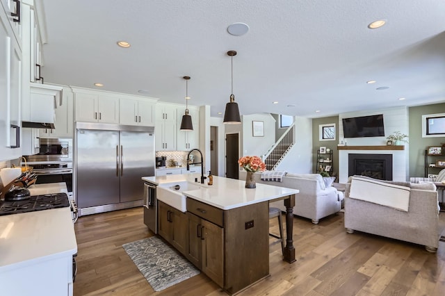 kitchen featuring light wood finished floors, built in appliances, light countertops, and a sink