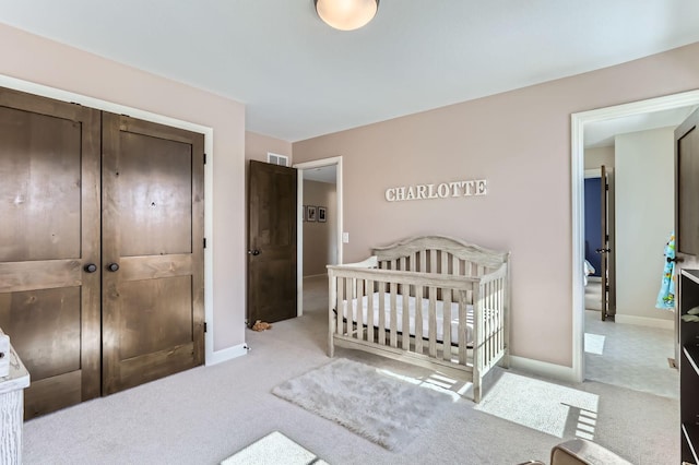 carpeted bedroom featuring a closet, baseboards, visible vents, and a crib