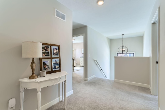 hall featuring visible vents, an upstairs landing, a notable chandelier, carpet flooring, and baseboards