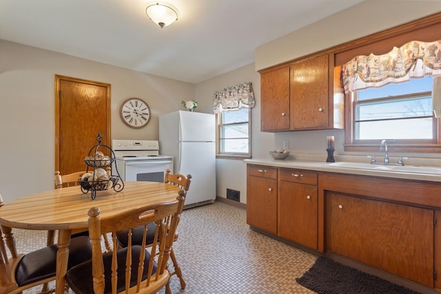 kitchen featuring a healthy amount of sunlight, light countertops, brown cabinetry, white appliances, and a sink