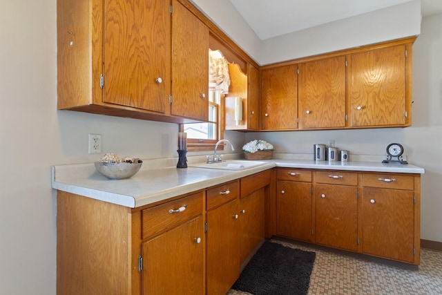 kitchen featuring brown cabinetry, light countertops, and a sink