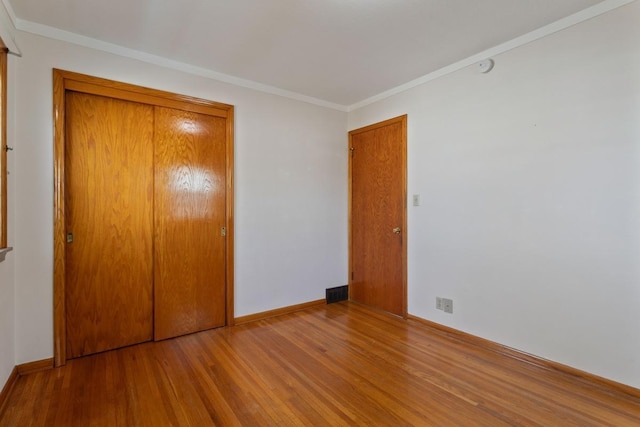 unfurnished bedroom featuring a closet, baseboards, wood finished floors, and ornamental molding