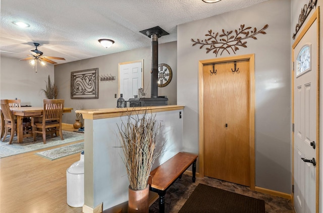 foyer entrance featuring baseboards, a textured ceiling, a wood stove, and a ceiling fan