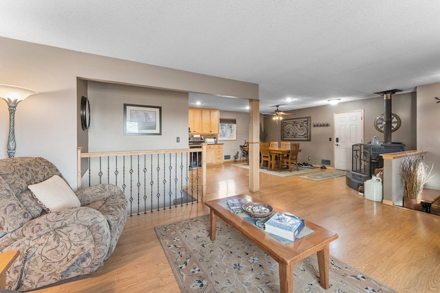 living area featuring light wood-style floors, ceiling fan, a wood stove, and a textured ceiling