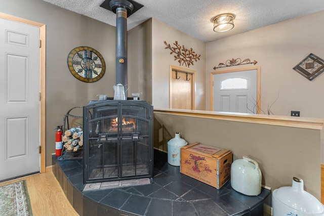 interior details featuring a fire extinguisher, a textured ceiling, wood finished floors, and a wood stove