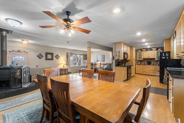 dining room featuring a textured ceiling, recessed lighting, light wood-style floors, ceiling fan, and a wood stove