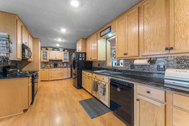 kitchen with black appliances, light brown cabinets, light wood-type flooring, and a sink