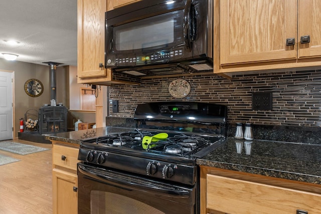 kitchen featuring tasteful backsplash, light brown cabinets, a wood stove, wood finished floors, and black appliances