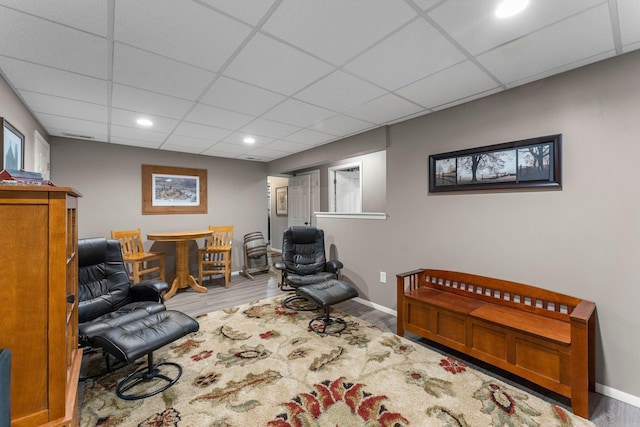 living area featuring a drop ceiling, baseboards, and wood finished floors