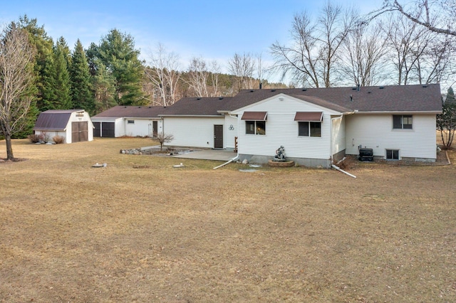 back of house with central AC unit, a lawn, an outbuilding, a storage unit, and a patio