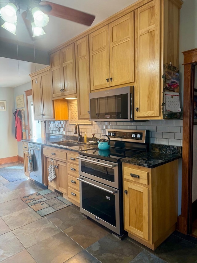 kitchen with baseboards, dark stone counters, a sink, stainless steel appliances, and backsplash