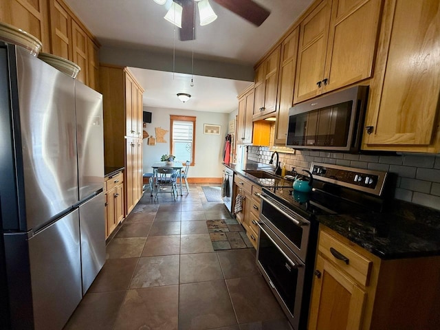 kitchen with backsplash, dark tile patterned floors, stainless steel appliances, a ceiling fan, and a sink