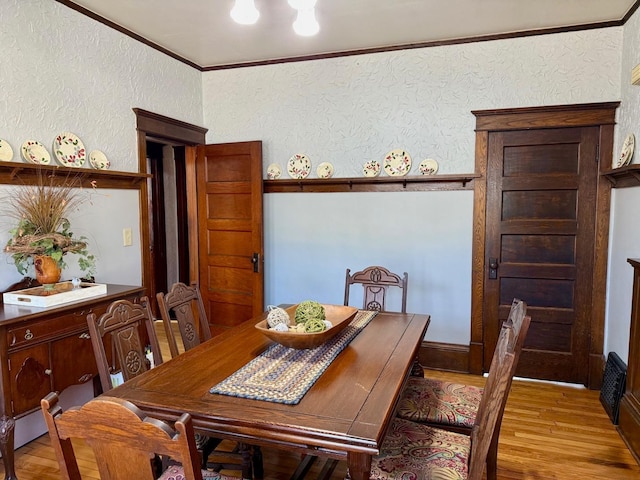 dining room featuring light wood-type flooring, crown molding, and a textured wall