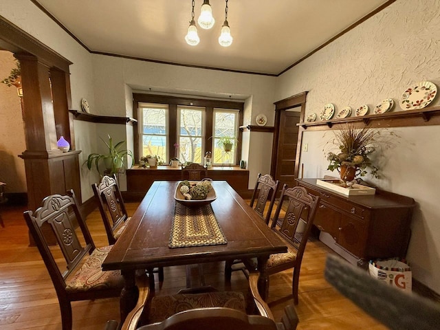 dining room with a textured wall, light wood-type flooring, ornamental molding, and decorative columns