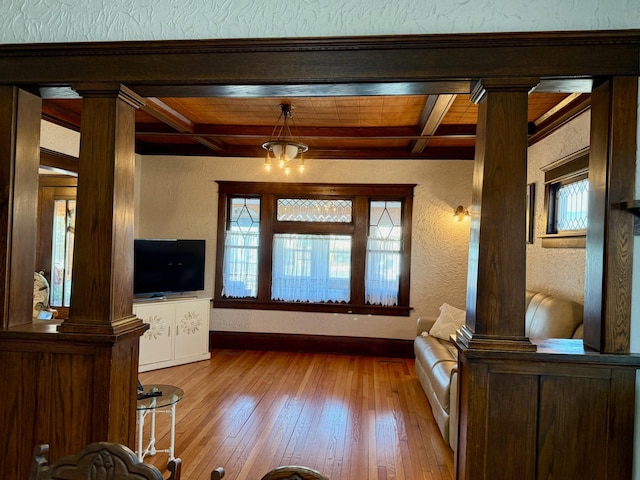 unfurnished living room with beam ceiling, hardwood / wood-style flooring, decorative columns, baseboards, and a textured wall