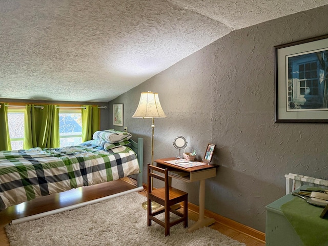 bedroom featuring lofted ceiling, a textured wall, baseboards, and a textured ceiling